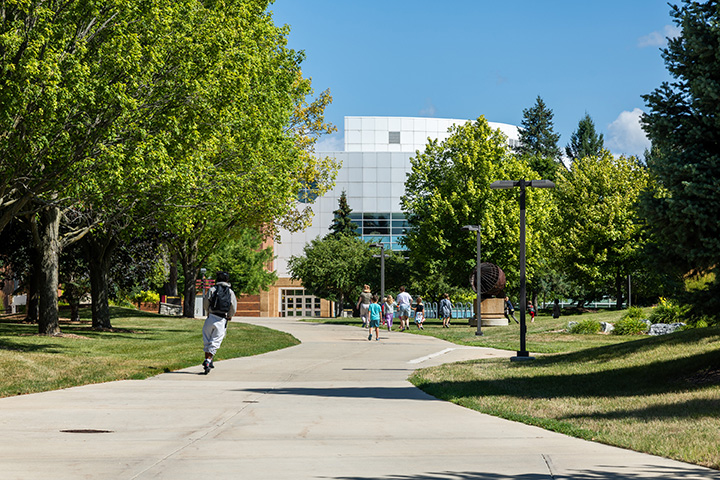 People walking and riding scooters down a pathway with the CMU Park Library in the distance