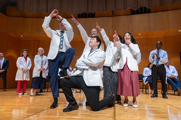 Medical students make a silly group photo pose while standing on a stage during the White Coat Ceremony