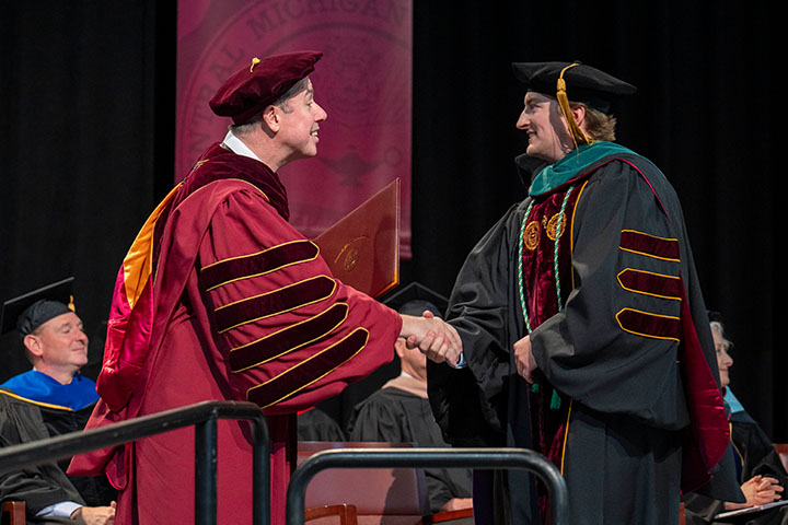 Men in graduation robes shaking hands.