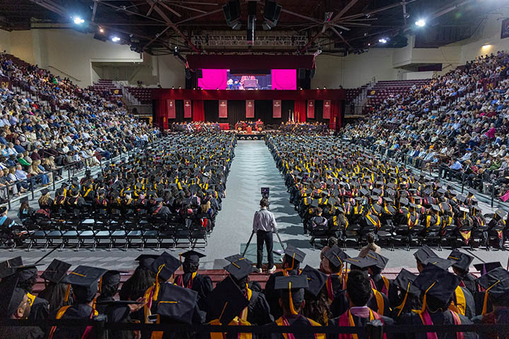 An arena full of people with robed graduates in the center.