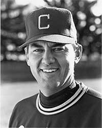 A black and white photo of a smiling man in a baseball hat with the letter C on it