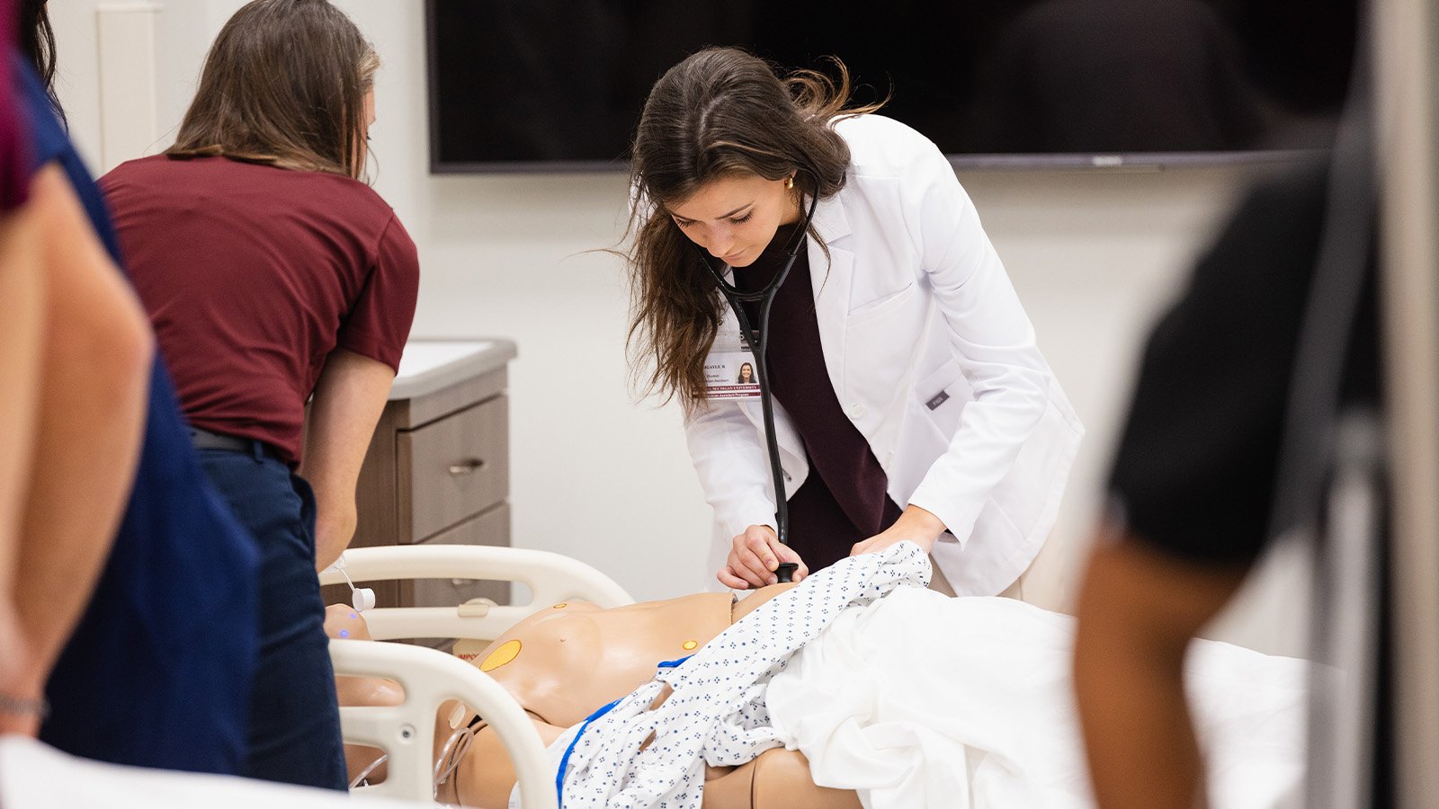 A brown haired female medical student works on a patient simulator in a hospital bed.