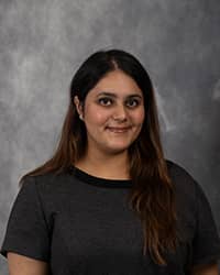Sadhya Sarin, Counselor Intern profile portrait, wearing a dark short sleeve shirt and long dark hair with a grey background.