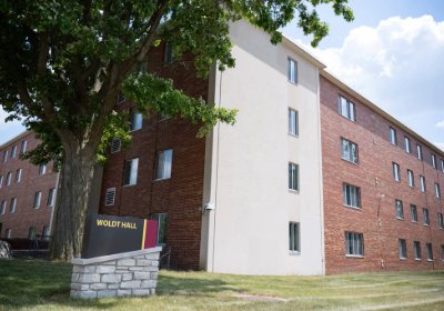 Woldt Hall sign in front of a red brick and cream concrete residence building, shaded by a large tree.