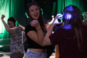 A group of people dancing at the silent disco for Fire Up All Night and wearing green lit up headphones.