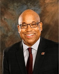 Professional headshot of Stan Shingles in a suit and tie against a brown and gray background