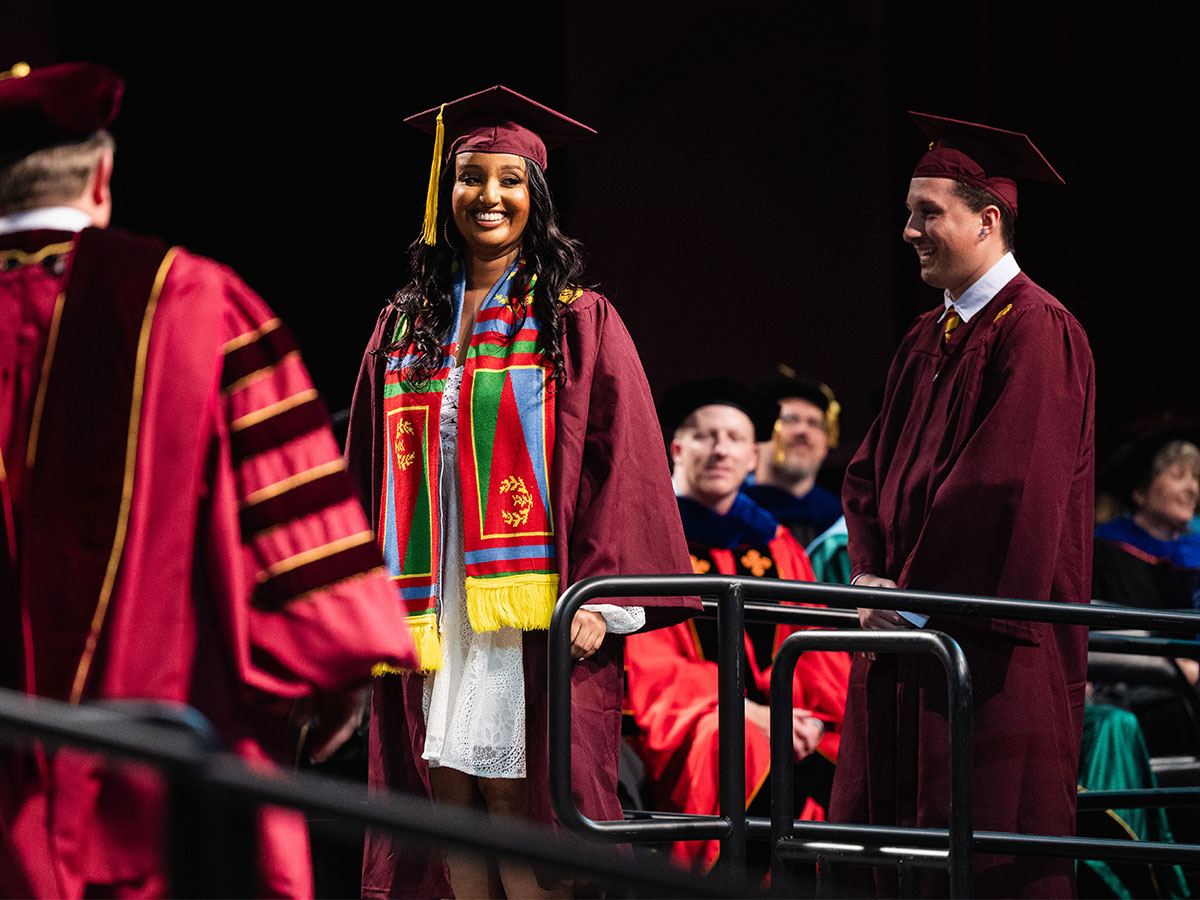 international_1200X900_4 Multiple students in their cap and gown on stage at commencement
