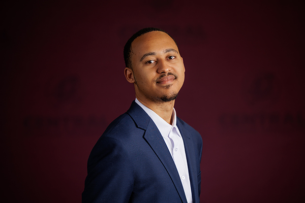 Professional headshot of Larry West, III wearing a white shirt and blue suit jacket on a maroon background.