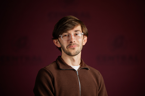 Professional headshot of Ryan Opperman wearing a brown sweater on a maroon background.