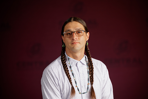 Professional headshot of Timothy Kern wearing a white button up shirt on a maroon background.