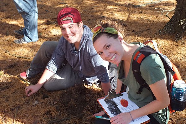 two students sitting on the ground doing homework looking up at the camera