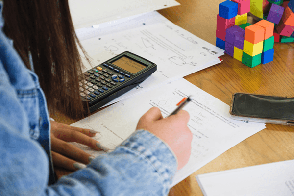 A student in a blue denim shirt sitting at a desk doing homework and using a calculator