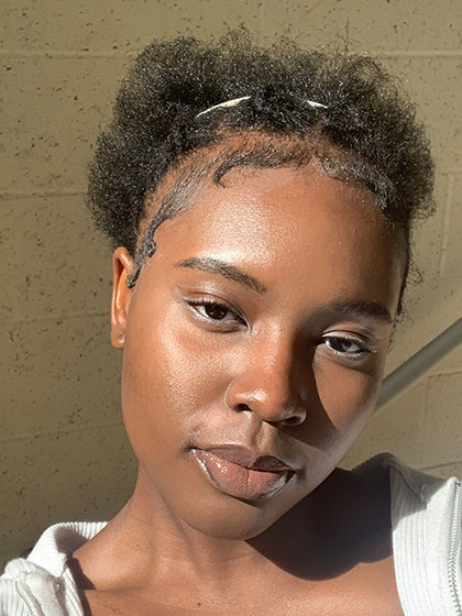 A headshot of SI Leader Eneni Alagoa posing in a white sweater in a stairway