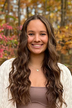 A photo of SI Leader, Madison Travis, posing outdoors in front of colorful fall foliage