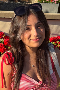 A photo of SI Leader, Mariah Zamora, posing outdoors in front of a bed of red flowers.