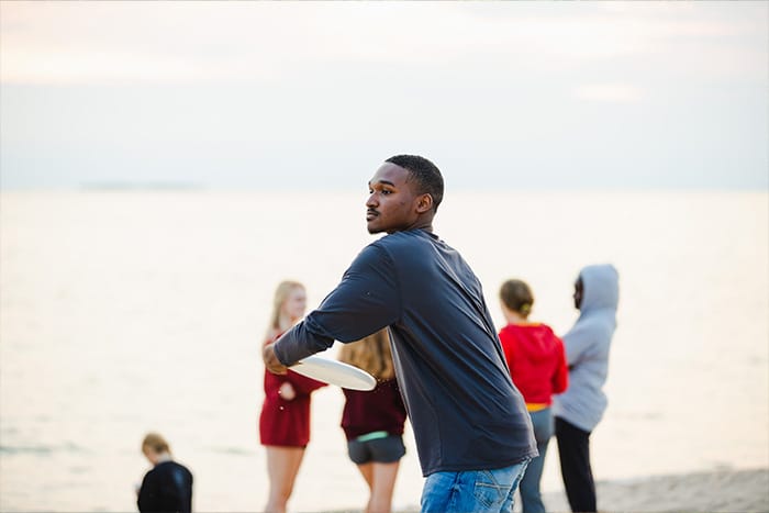 A student in a blue long sleeve shirt throws a frisbee on the beach at Beaver Island.
