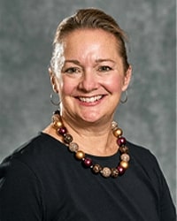 Alumni Board member Catherine Claes in a black top with a large beaded necklace and her blonde hair is pulled back into a bun.