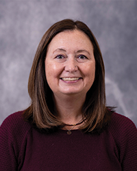 A woman smiling at the camera in a maroon top and medium length brown hair. She is in front of a gray portrait backdrop.