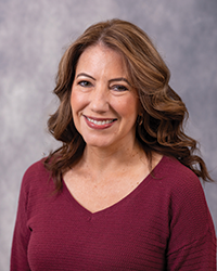 Alumni Board member Lisa Bottomley smiles for a portrait, wearing a maroon top and she has long brown hair.