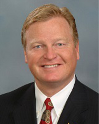 Robert Van Deventer is an Alumni Board member who holds Emeritus status and he is wearing a black suit and a red and gold tie and he has short hair.