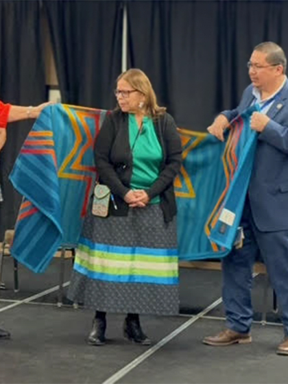A woman stands with a blanket behind her that's being held by someone on each side.