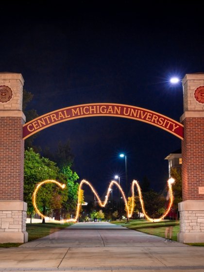 CMU's arch on campus at night, showing the trace of a sparkler firework beneath it spelling letters "CMU".