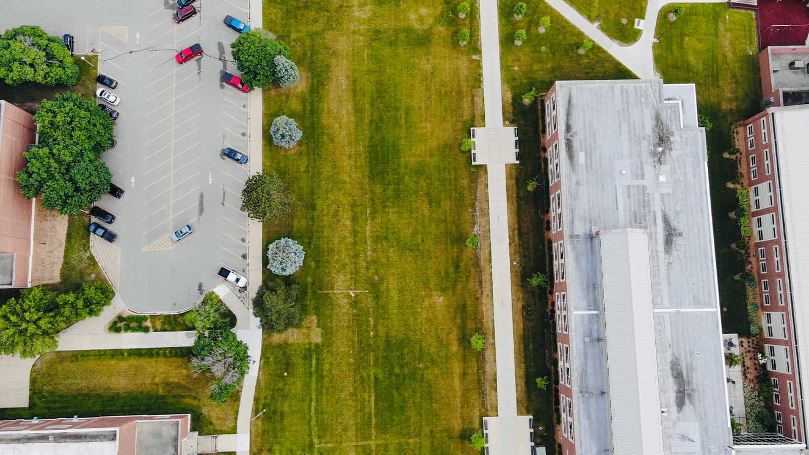 a parking lot with cars parked in it sits next to a lawn with buildings on the other side