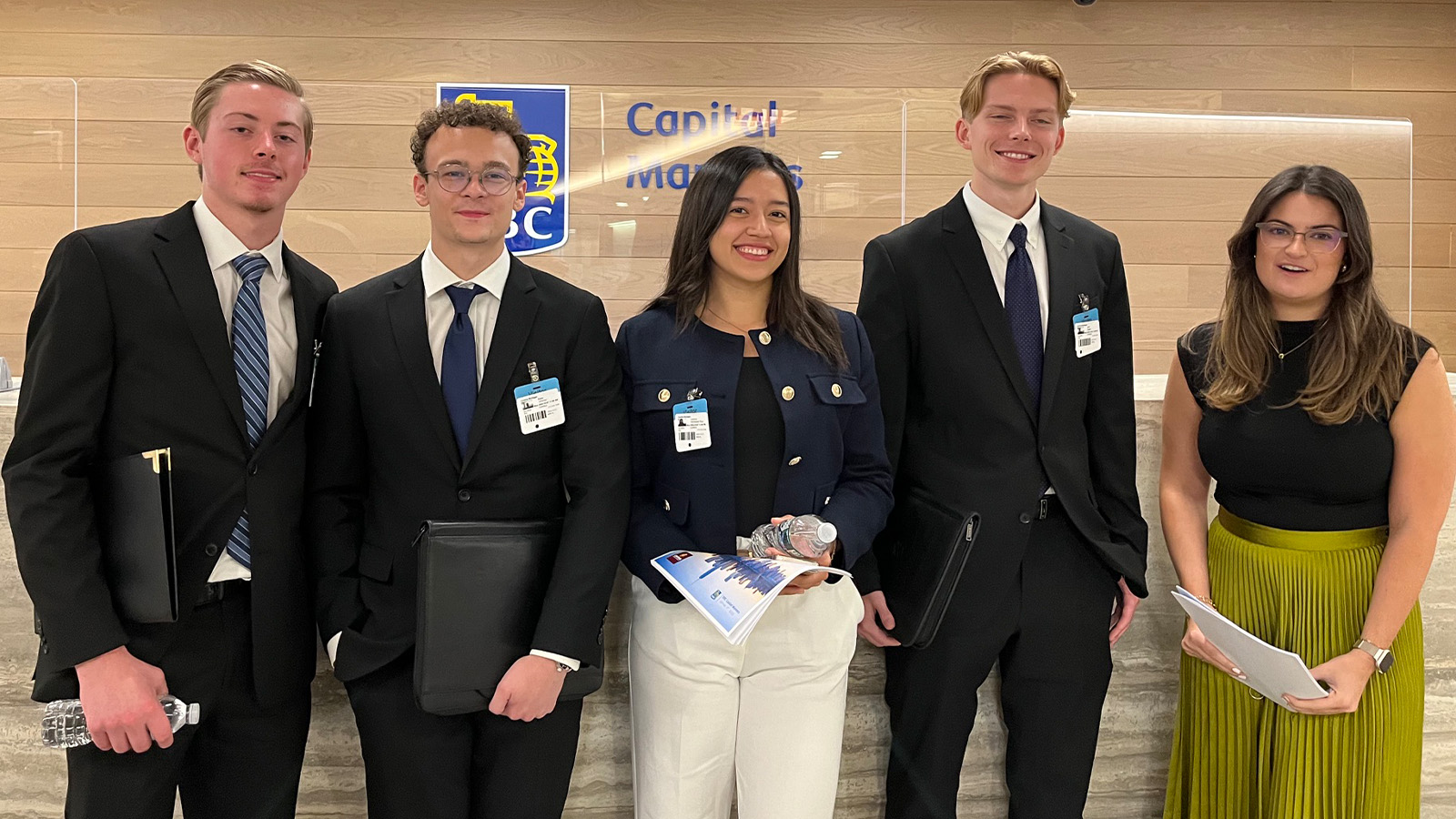 A group of college students dressed up in professional clothes stand in front of a wall.