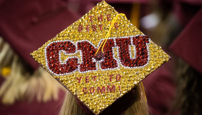 A CMU graduate wearing a decorated graduation cap with sparkling letters and text saying 'The Best Is Yet to Comm!' and 'CMU'.