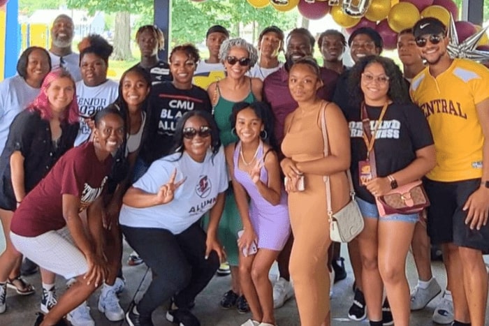 A large group of people wearing maroon and gold pose together at an outdoor event.