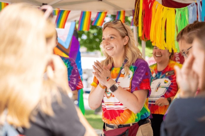 A Central Michigan University staff member in a rainbow t-shirt talks with visitors of the booth.