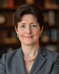 A woman with short dark hair wearing a suit and gold necklace.