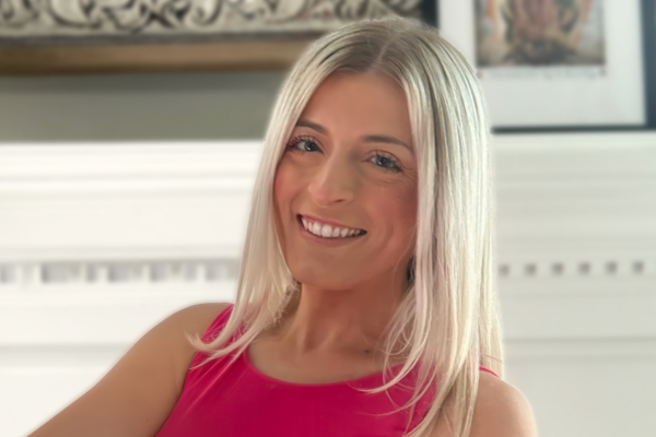 A woman with blonde hair and a pink tank top smiles at the camera.