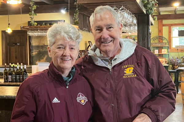 A man and woman wearing maroon jacket. The woman's has an Adidas logo showing and the man's has a Central Michigan logo.