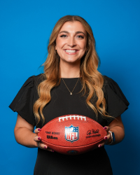 A woman with long light brown hair is wearing a black dress and holding an official Wilson NFL football in front of her.