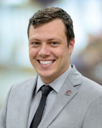 Nicholas Bogen 200x250 A man with glasses and short brown hair smiles while wearing a dark suit, navy blue tie and light blue shirt.