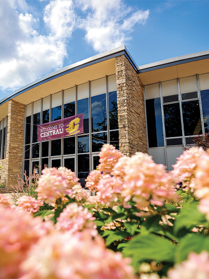 Close up of peach and white flowers in front of a building with a sign in front of the windows that reads Welcome to Central!