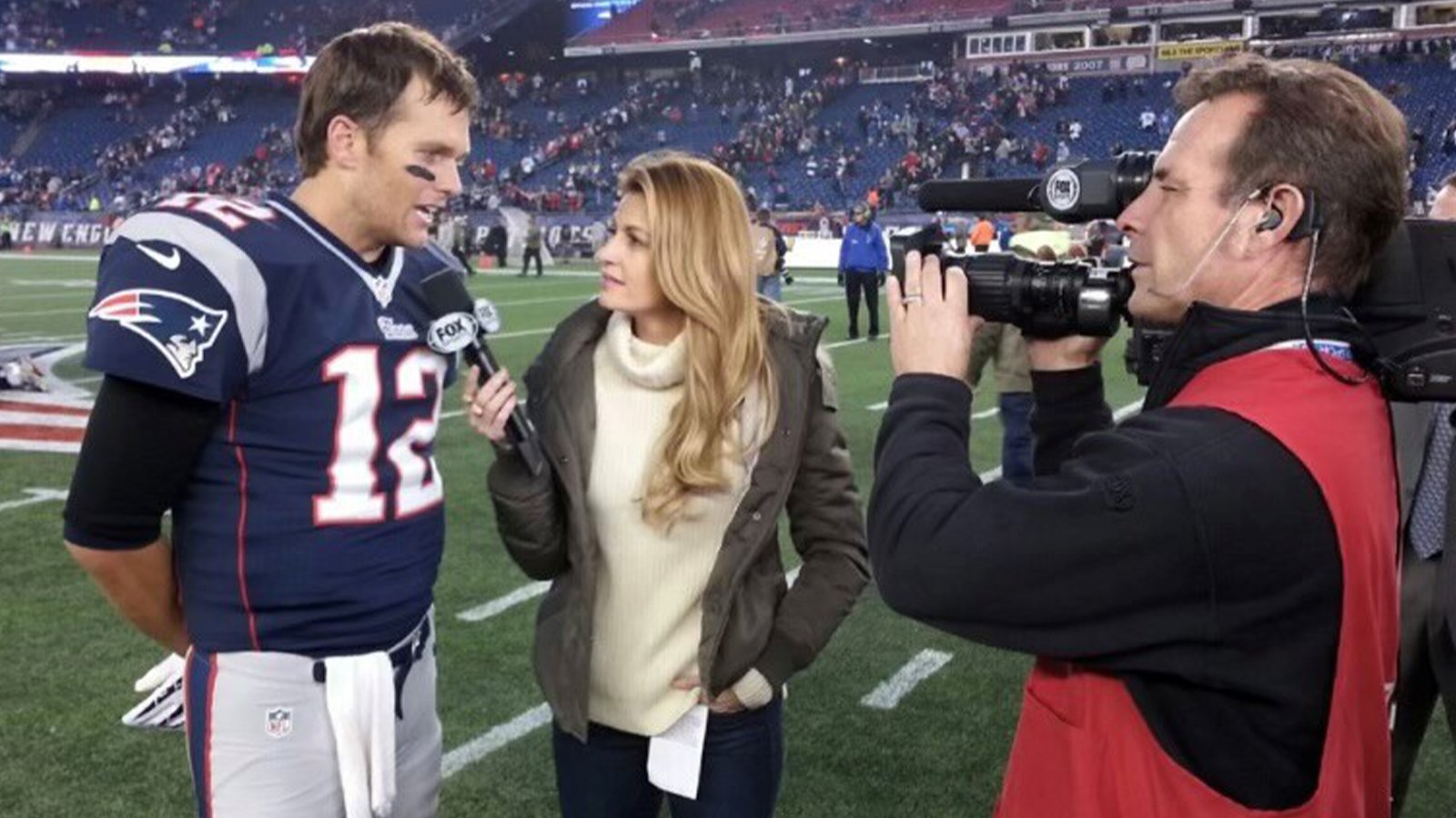 A cameraman captures a video of a football player being interviewed by a woman on a football field.