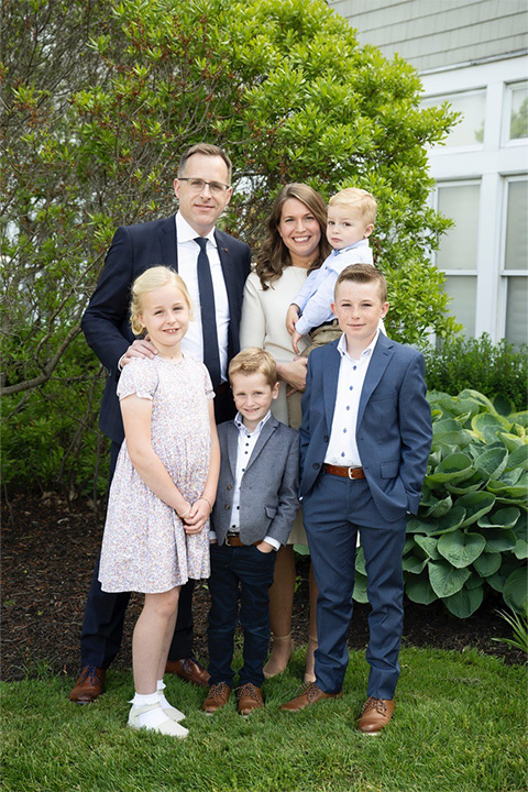 Family portrait in front of bushes of a man, woman and four children.