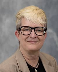 Brie Walter, Director of Sexual Aggression Services Brie Walter, Director of Sexual Aggression Services profile portrait, wearing black framed glasses, black shirt with beige jacket, and a grey background