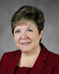 Cowling-K-200x250 A woman with short dark blonde hair poses for a headshot swearing a red blazer.